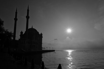 Silhouette of buildings by sea against sky and fog