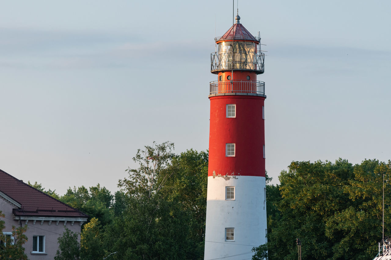 LIGHTHOUSE AMIDST TREES AND BUILDINGS AGAINST SKY