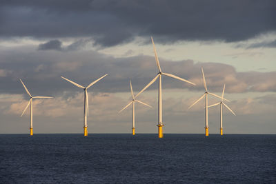 Wind turbines by sea against sky