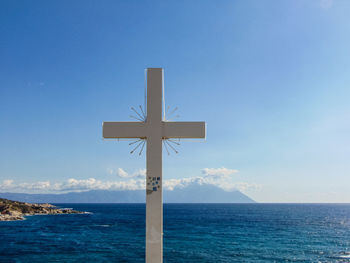Cross on sea against blue sky