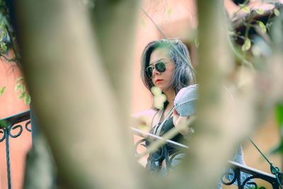 Low angle view of woman wearing sunglasses seen through branches