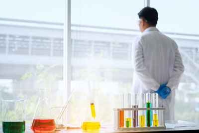 Rear view of scientist standing by window at laboratory