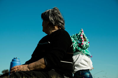 Low angle view of woman with granddaughter against clear blue sky