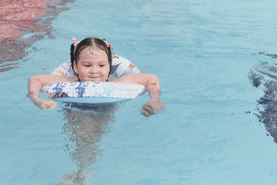 Happy asian little girl swimming in rubber ring, having fun in open air thermal pool.