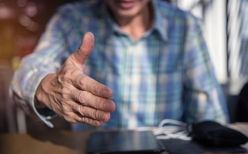 Midsection of man offering handshake while sitting at table