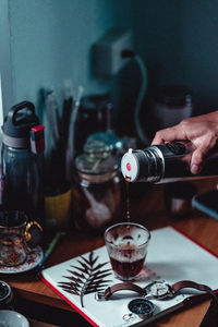 Midsection of person pouring drink in glass on table