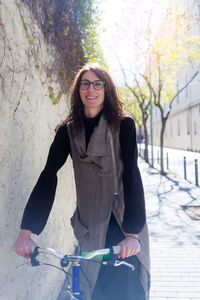 Young smiling woman walking on a city street with bicycle