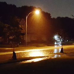 Illuminated street light by road against sky in city at night