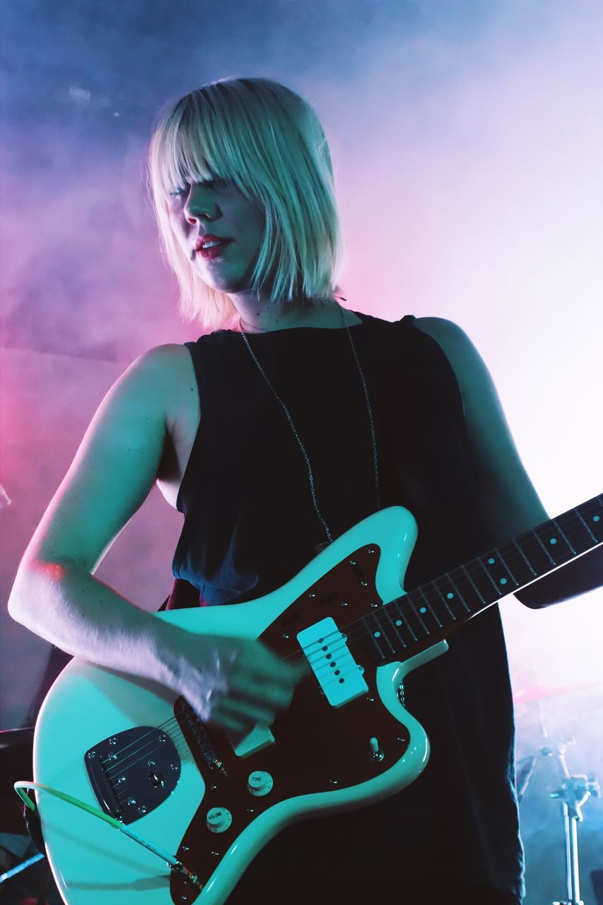 lifestyles, leisure activity, music, casual clothing, arts culture and entertainment, person, musical instrument, three quarter length, technology, guitar, young adult, standing, waist up, communication, wireless technology, indoors, hobbies, holding