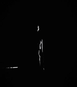 Silhouette person by illuminated light against black background