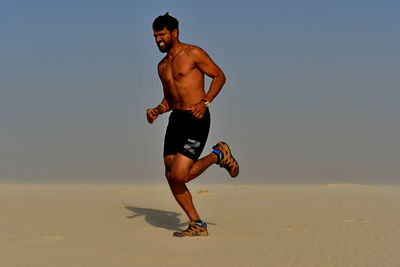 Full length of shirtless man running on beach