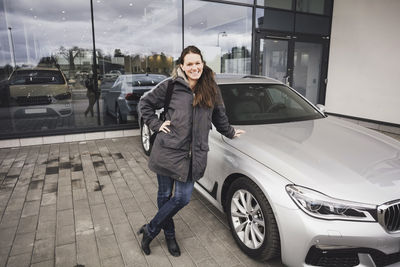 Portrait of smiling woman standing by car against showroom