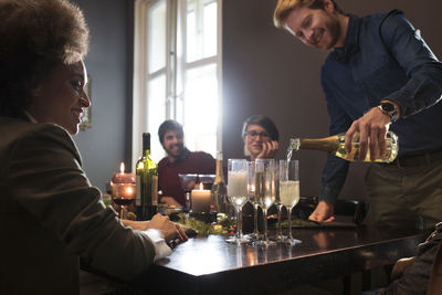 Man pouring champagne in glasses for friends during christmas party