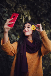 Close-up of woman taking selfie wearing flower in hair standing outdoors