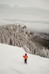 Rear view of man walking on snow covered mountain against sky