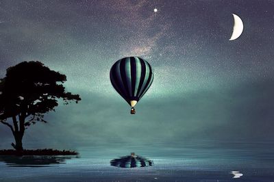 Hot air balloons in sea against sky at night