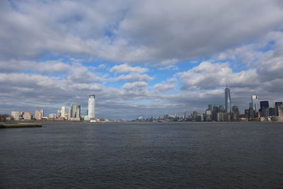 City buildings at waterfront against cloudy sky