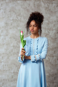 Sad young woman holding flower while standing against wall