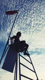 Low angle view of silhouette woman sitting against sky