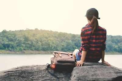 Rear view of woman sitting on rock against lake