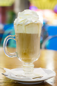Glass cup of coffee latte with whipped cream on wooden table