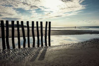 Wooden posts on beach against sky