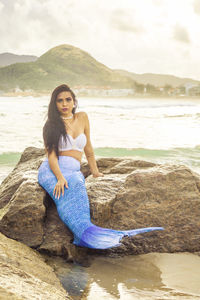 Portrait of young woman sitting on shore against sea