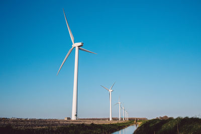 Windmill on field against clear blue sky