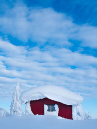 Red house on snow covered landscape against sky