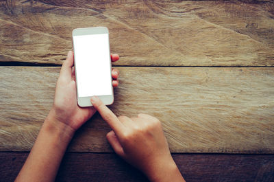 Cropped hands using blank phone at wooden table