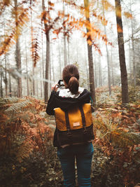 Back view of woman with backpack in a beautiful forest full of fog and taking photos with compact camera in basque country, spain