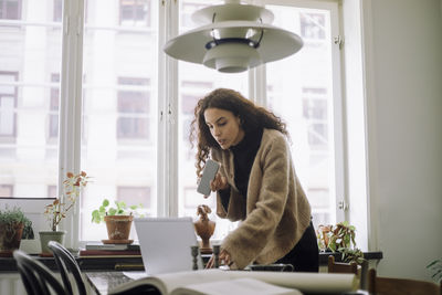 Busy female design professional doing multi-tasking with smart phone and laptop while working at home office