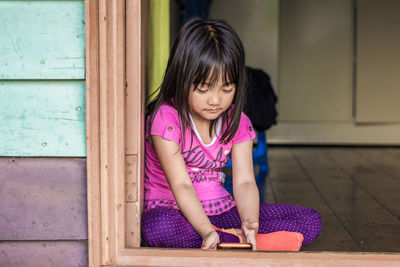 Portrait of cute girl sitting against pink wall