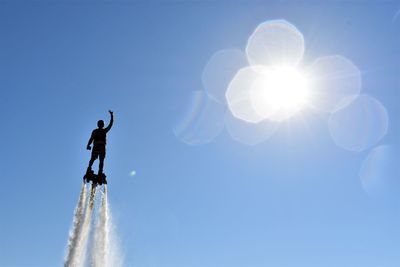 Low angle view of man flyboarding against clear blue sky