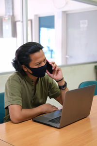 Man wearing flu mask talking on phone in office