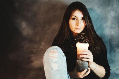 Portrait of young woman holding candles sitting against wall
