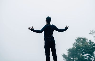 Rear view of man with arms outstretched standing against clear sky