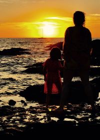 Rear view of silhouette people on beach during sunset