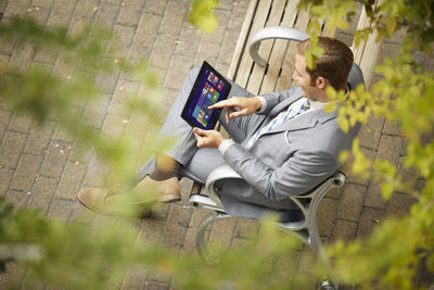 Side view of man using mobile phone while sitting on plant