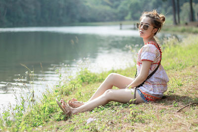 Side view of woman sitting on grass by lake