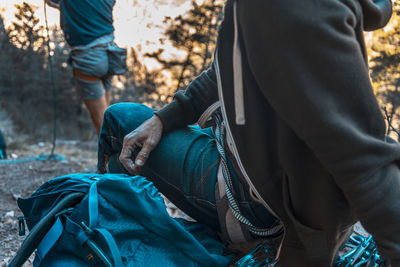 Midsection of man sitting in forest during sunset