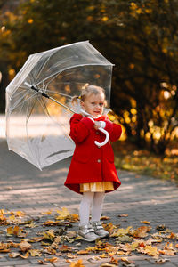 Cute girl holding umbrella while standing outdoors