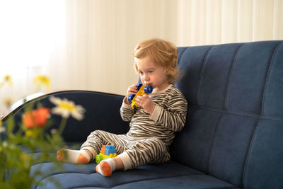 Cute girl playing with toy sitting on sofa at home