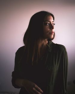 Young woman looking away while standing against wall