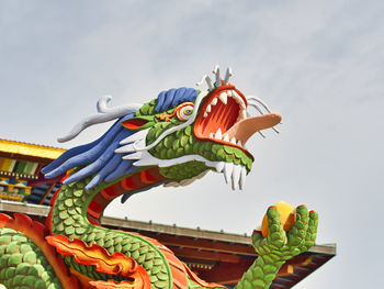 Low angle view of multi colored bird on building against sky