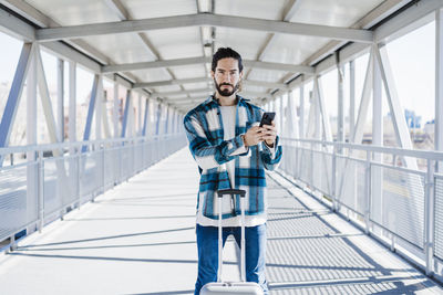 Young man using mobile phone while standing on railing