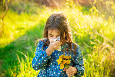 Girl holding flower blowing nose with tissue