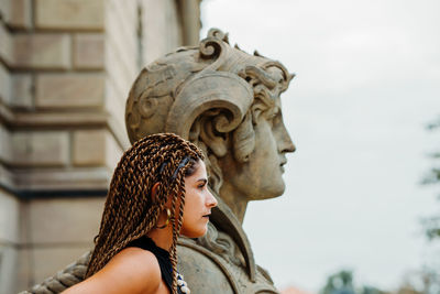 Close-up of woman looking away while standing by statue against historic building