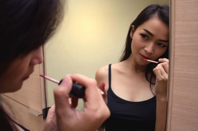 Woman applying lipstick while looking into mirror at home