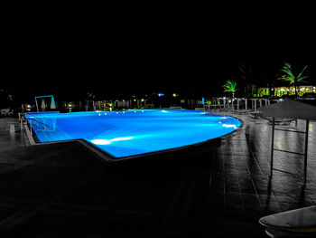 Illuminated swimming pool in city against sky at night